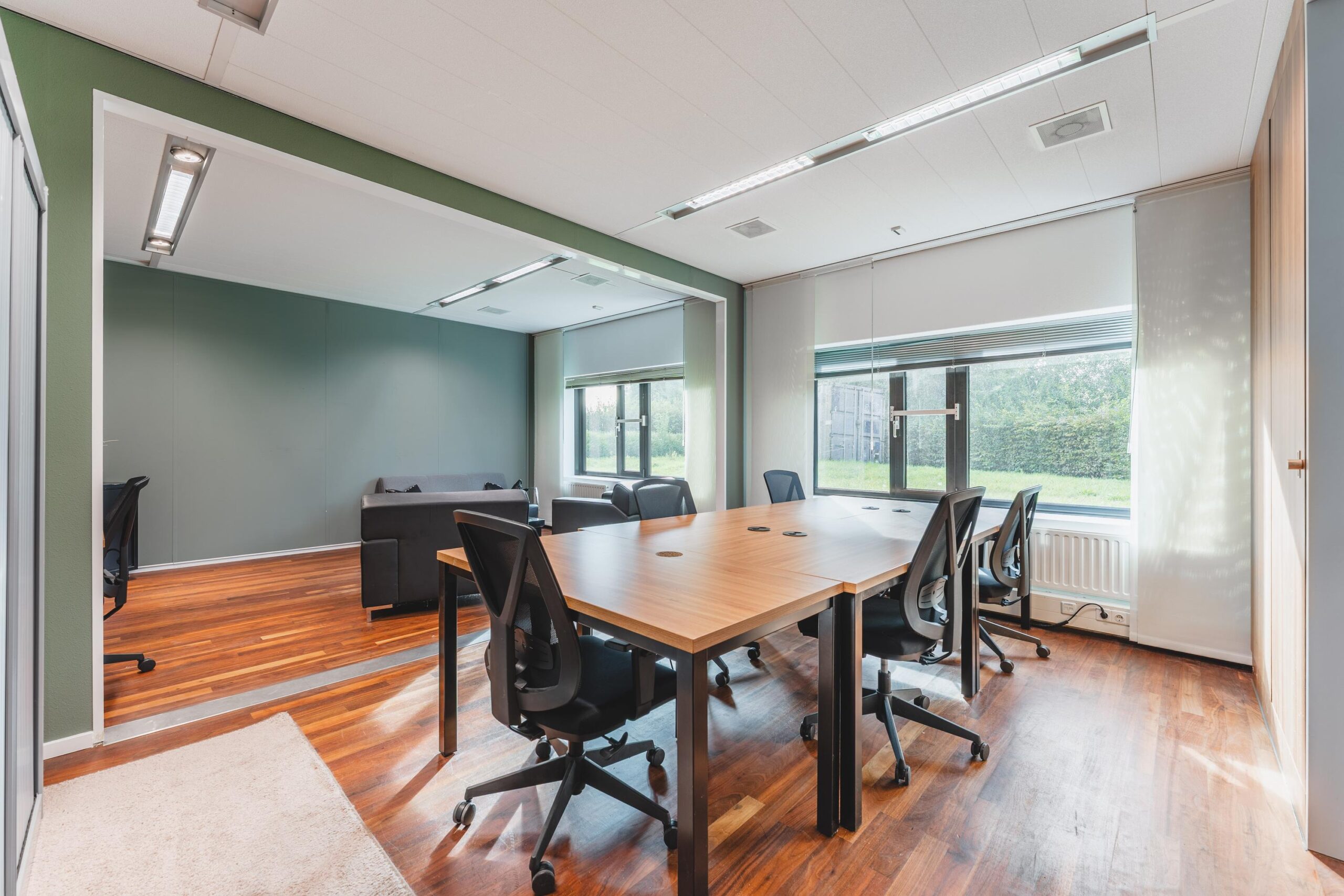 Moderne vergaderruimte aan de Prof. W.H. Keesomlaan met houten vloer, grote ramen en ergonomische bureaustoelen rondom een grote tafel.